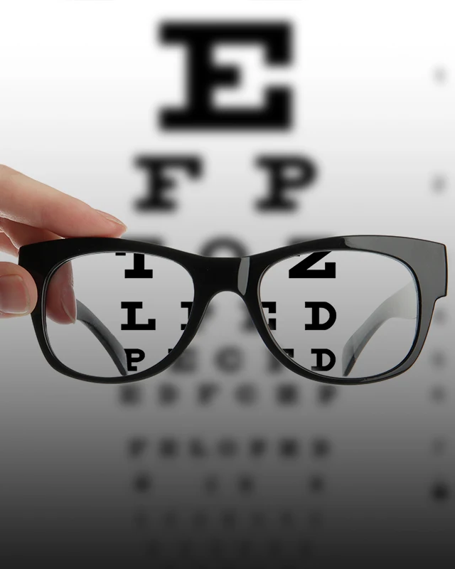 Hand holding pair of eye glasses with an eye chart behind them